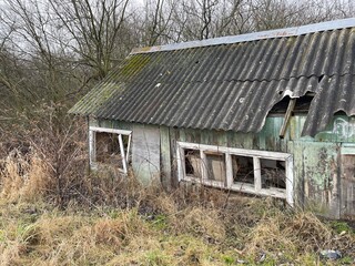 Abandoned Wooden Structure With Broken Windows and Overgrown Vegetation in a Rural Area During...