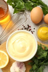 Delicious mayonnaise sauce in bowl, whisk and ingredients on grey table, flat lay