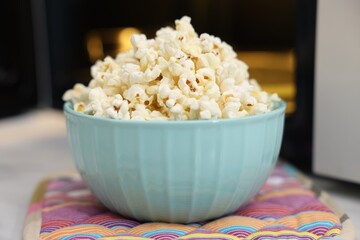 Tasty popcorn in bowl near microwave oven on table, closeup