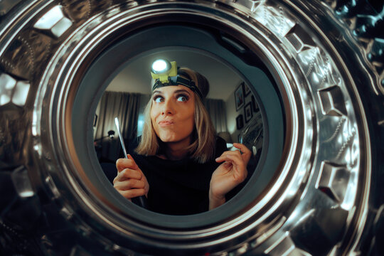 Woman with a Flashlight Trying to Repair her Washing Machine. Housewife trying to fix her electrical appliance all by herself 
