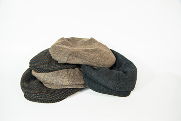 Pile of newsboy hats and scally caps with assorted different colors and patterns on a white background. Concept photo of stack of classic irish hats in white studio