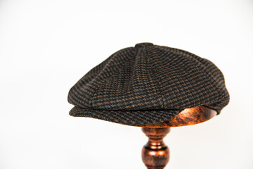 Concept photo of a newsboy cap made of black herringbone wool fabric mounted on a bronze mannequin head. Product catalog photo of a classic newsboy cap isolated on a white background