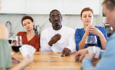 Interested African American man playing poker with group of friends in relaxed home atmosphere around kitchen table