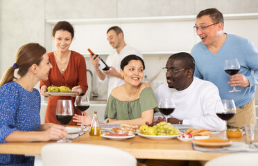 Fototapeta premium Happy adult friends at the festive table discussing the news and drinking red wine