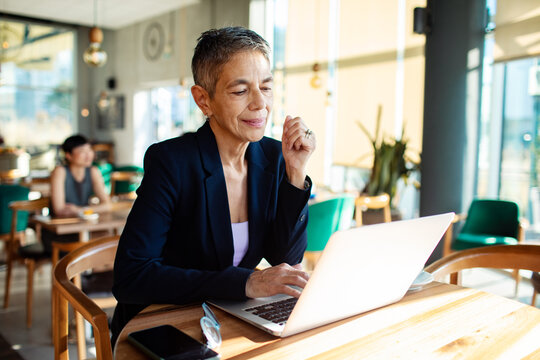 Mature businesswoman working on laptop in modern cafe