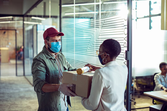 Delivery man handing package to office worker in modern workspace