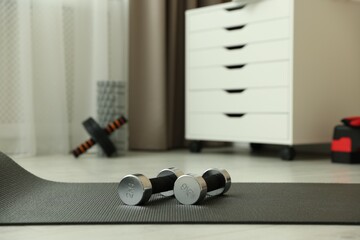 Metal dumbbells and mat on floor indoors