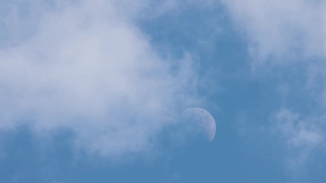青い空に浮かぶ白い半月とゆっくり流れる雲