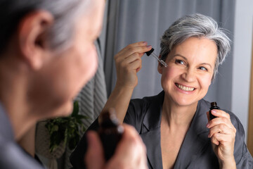 An beautiful woman of age during menopause with gray hair applies hormonal serum against wrinkles
