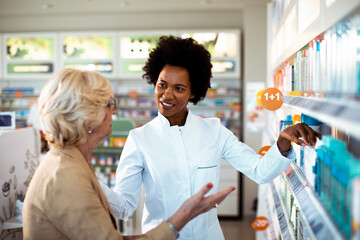 Black female pharmacist assisting senior customer in modern pharmacy