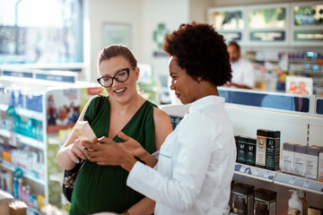 Pharmacist helping pregnant woman with product in drug store
