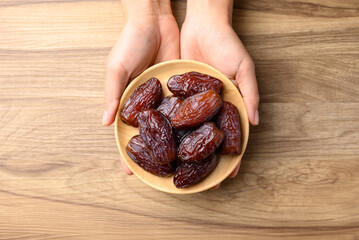 Date palm fruit (MedJool) on wooden plate holding by hand, Table top view