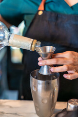 A skilled bartender pours a crafted drink into a shaker with a funnel, showcasing their expertise