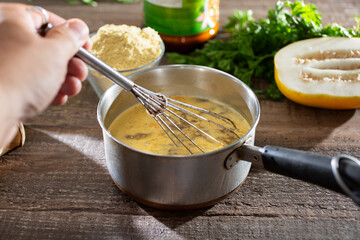 A view of a hand using a whisk to stir chicken bouillon powder into a water in a saucepan.