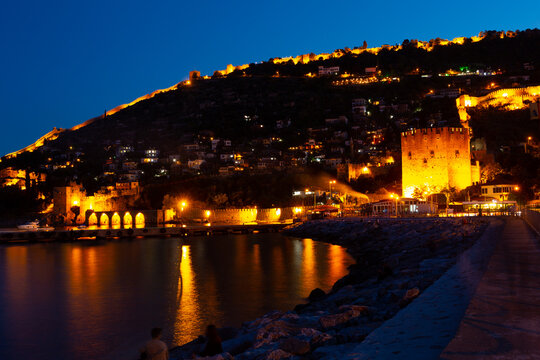 Illuminated Mediterranean coast of Alanya, Antalya Province, Turkey. View of Red Tower and Tersane dockyard in evening.