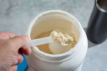 A view of a hand scooping some vegan protein powder out of a large container.