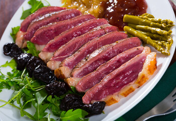 Slices of fried duck magret with sauces, prune and vegetable garnish of pickled asparagus and fresh greens