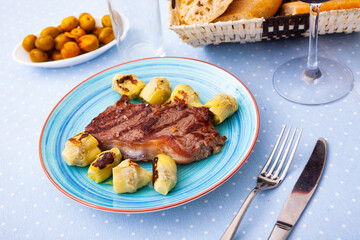 Delicious veal steak with fried artichokes on a blue plate