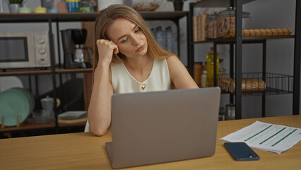 Woman blonde working on laptop indoors looking thoughtful in modern workplace surrounded by...