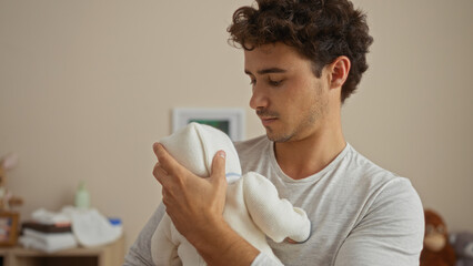 Young man holding baby in bedroom, showcasing tender interaction indoors with attractive, hispanic...