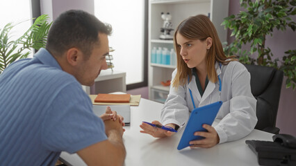 Obraz premium Woman doctor discussing with man patient in a clinic room, both engaged over a digital tablet, highlighting the modern healthcare setting indoors.