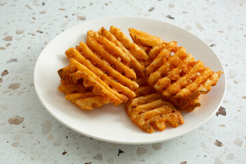 A view of a pile of waffle fries on a plate.