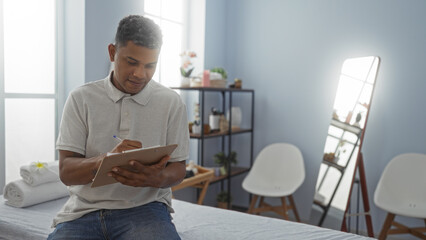 Handsome young man writing on clipboard in a well-lit rehab clinic room with modern decor and a pleasant ambiance