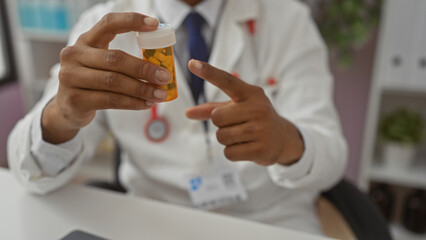 Young man in clinic points to a medicine bottle, showcasing hispanic healthcare professional in a hospital setting, emphasizing medical expertise and patient care.