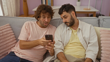 Men sitting on a couch indoors looking at a smartphone together in a living room implies a strong bond of friendship and family, enjoying their time in a cozy apartment.