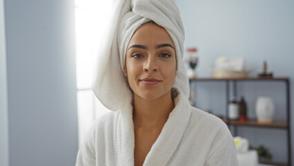 Young woman with towel and robe in a spa room, showcasing a relaxed and attractive appearance in a wellness salon interior.