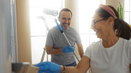 Hispanic couple painting their new home together, enjoying the process in a bright living room,...