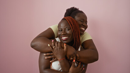 Two smiling african american women in a loving embrace against a pink background, exemplifying sisterhood, friendship, and familial love.