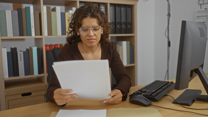Fototapeta premium Woman working at desk in office holding documents serious expression female employee focused reading papers