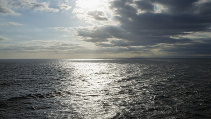 Fototapeta premium Ocean reflecting sunlight under a cloudy sky with horizon visible in the distance, creating a dramatic and serene seascape in a natural outdoor setting.