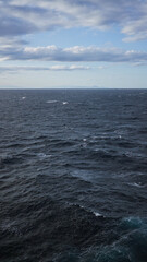 Ocean waves under cloudy sky with distant islands visible on the horizon showcasing a serene seascape under blue cloudy skies during the daytime, capturing a sense of tranquility and vastness.