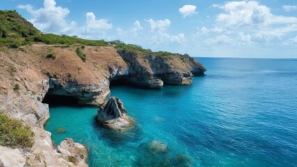 Fototapeta premium Tranquil Coastal Landscape with Turquoise Water, Blue Sky, and Rocky Cliffs with Green Vegetation and Cavelike Formations.