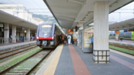 Blurred train arriving at busy station platform with defocused passengers under open roof during...