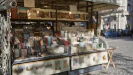 Blurred outdoor kiosk displaying various books and magazines on a sunny street with defocused background and bokeh effect, capturing an urban european atmosphere.