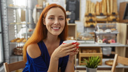 Smiling woman enjoying coffee at a bakery indoors with shelves of bread and pastries in the background