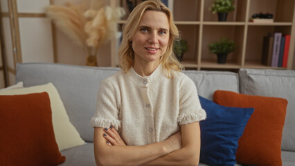 Obraz premium Woman smiling with crossed arms in cozy living room with stylish decor, framed by shelves and cushions, creates serene atmosphere at home.