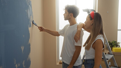 Man and woman painting wall in new home living room, showcasing couple teamwork and love indoors, with clear natural light enhancing fresh, modern interior.