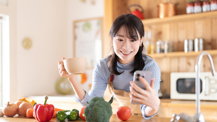 キッチンでスマホを見るエプロン姿の女性