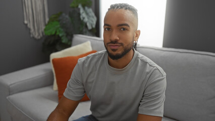 Young man with braids sitting in a stylish living room setting, showcasing modern indoor decor and a relaxed atmosphere in an apartment.