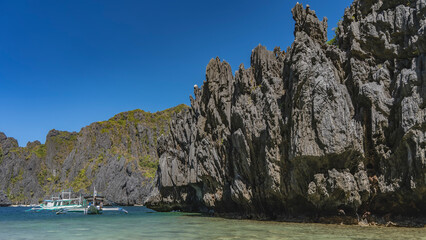 Picturesque karst cliffs surround the turquoise lagoon. Green vegetation on steep furrowed slopes....