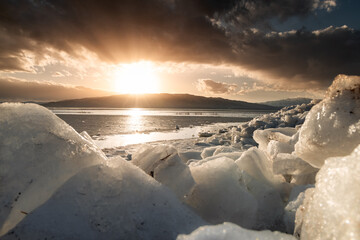 Ice stacks in foreground at Vineyard Beach on Utah Lake in Utah at sunset in February 2025.
