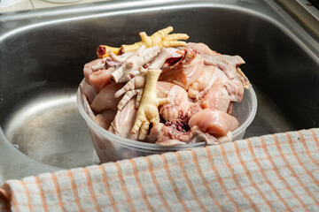 Cuts of raw chicken parts in a large bowl in the kitchen sink, which will later be cleaned