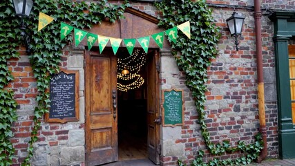 A welcoming entrance to a charming pub featuring rustic wooden doors, ivy-covered brick walls, and decorative banners. Soft lighting inside creates an inviting atmosphere for patrons.