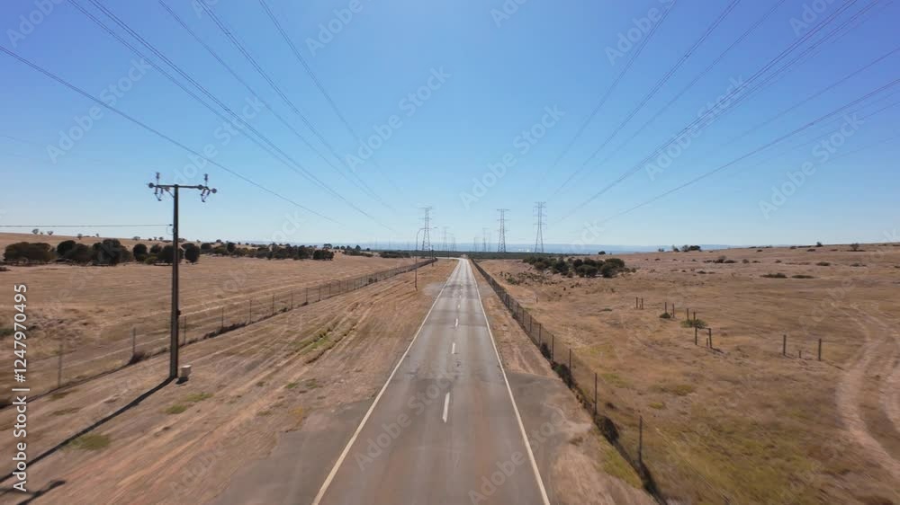 Poster drone flying forward and rising above a empty paved road with high power lines on each side in a dry