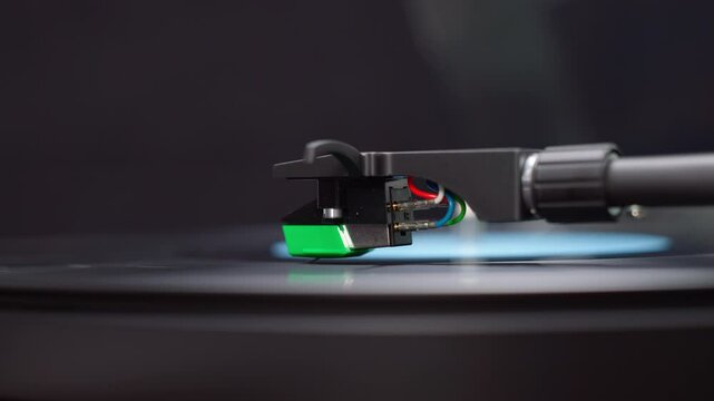 A macro close-up of a turntable needle rising from the dead wax area of a black vinyl record. The stylus hovers delicately, signaling the vinyl's end.