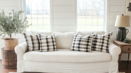 Fototapeta premium Cozy living room with white sofa, black and white plaid pillows, olive tree, and large windows.